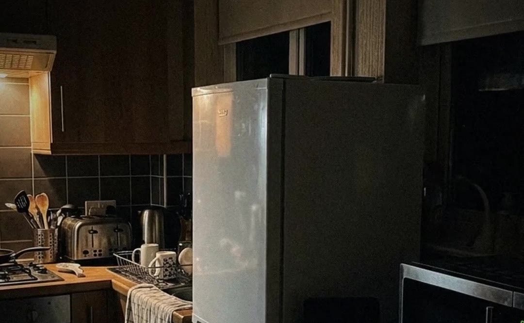 A British kitchen in the evening with a fridge-freezer, a broadband router and an energy bill on the table